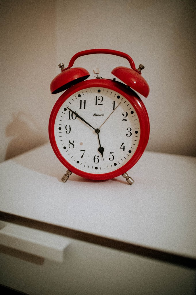 A red analog alarm clock on a white surface