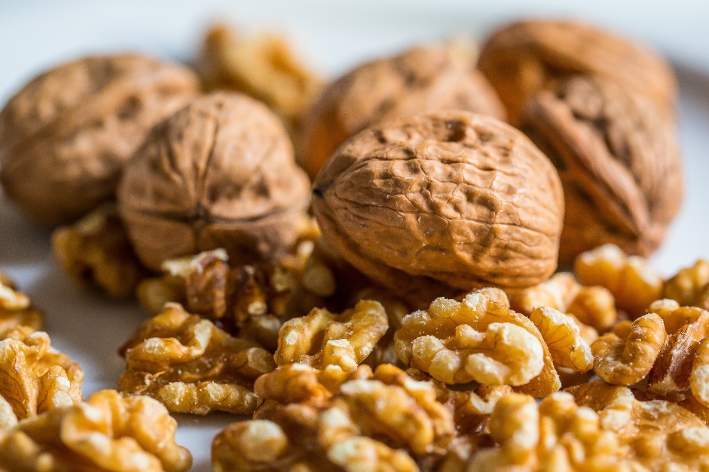 Whole walnuts in their shells beside a pile of shelled walnut pieces on a light surface